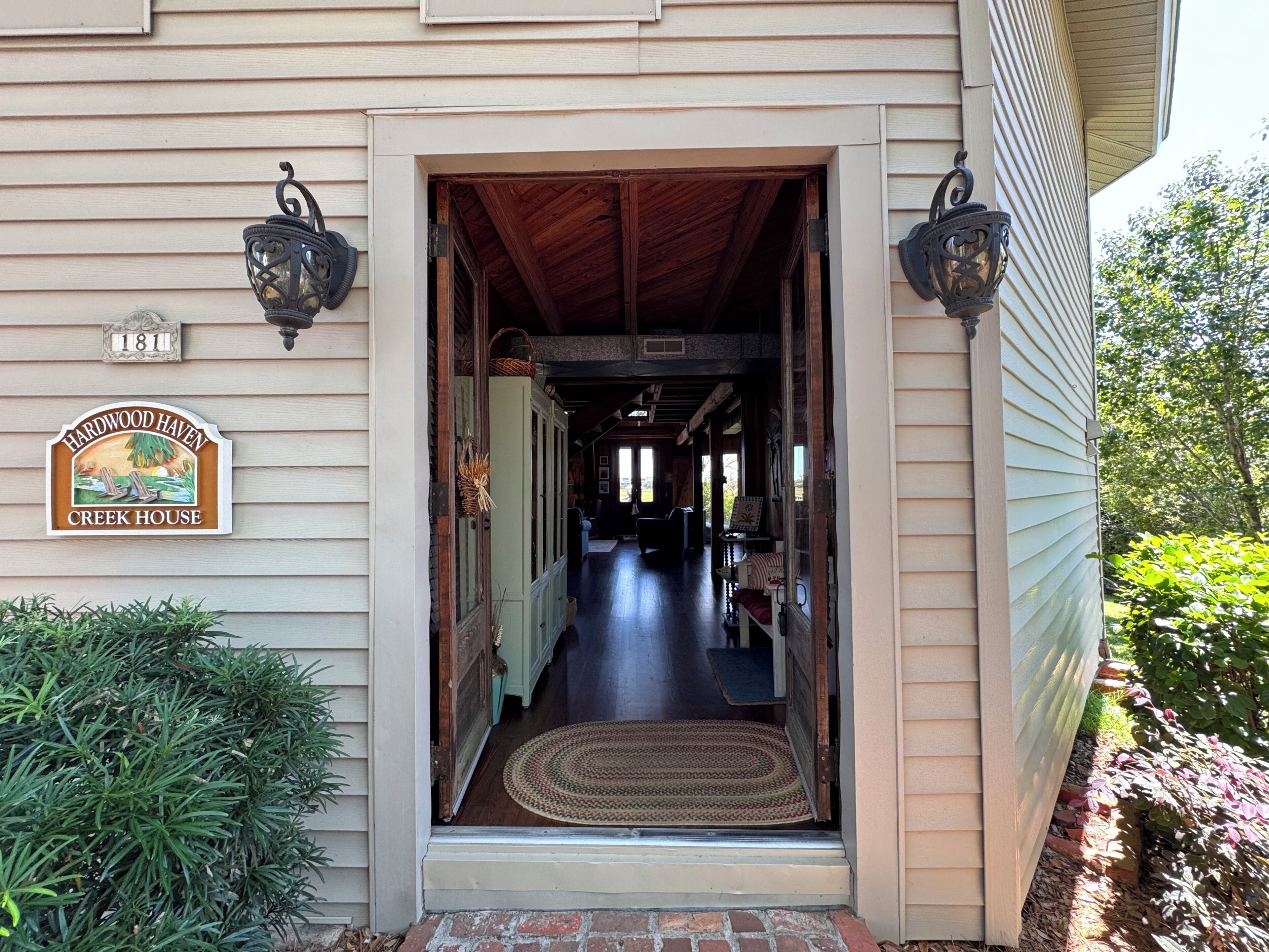 A house entrance with a wooden door, a doormat, and a sign indicating 'Creek House.'