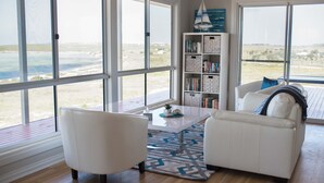 A spacious living room with large windows, a white sofa, a coffee table, and a bookshelf.