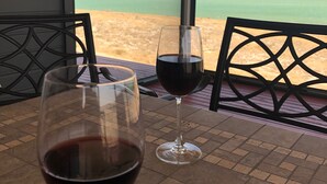 A table with two wine glasses, one with wine, and a view of a beach and water.