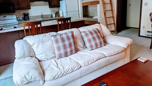 Ein Wohnzimmer mit einem weißen Sofa, karierten Kissen, einem Holztisch und einer Fernbedienung.