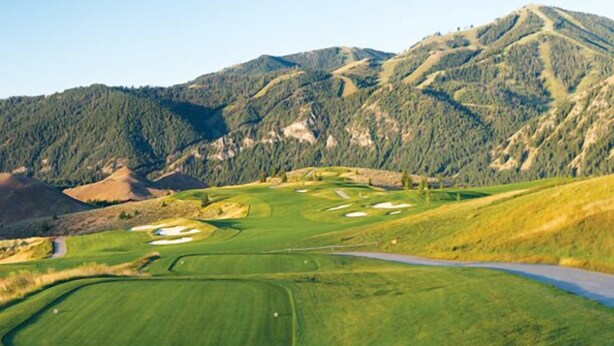 Ein Golfplatz mit einer daran entlangführenden Straße, umgeben von bewaldeten Bergen.