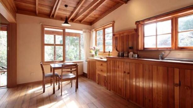 Una cocina de madera con una mesa de comedor y sillas, ventanas amplias y armarios de madera.