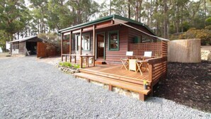 Una cabaña de madera con un porche, una pequeña terraza y un área cercada.