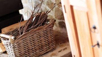 Un panier en osier rempli de branches, posé sur une surface en pierre, à côté d’une armoire en bois.