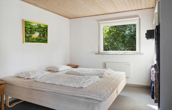 A bedroom with a bed, a window with a view of greenery, a radiator, and a painting on the wall.