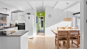 A modern kitchen with white cabinets and a black countertop, a dining area with wooden chairs and a table, and a hallway with a green accent wall. - Pet friendly home in Væggerløse with WiFi (Væggerløse)