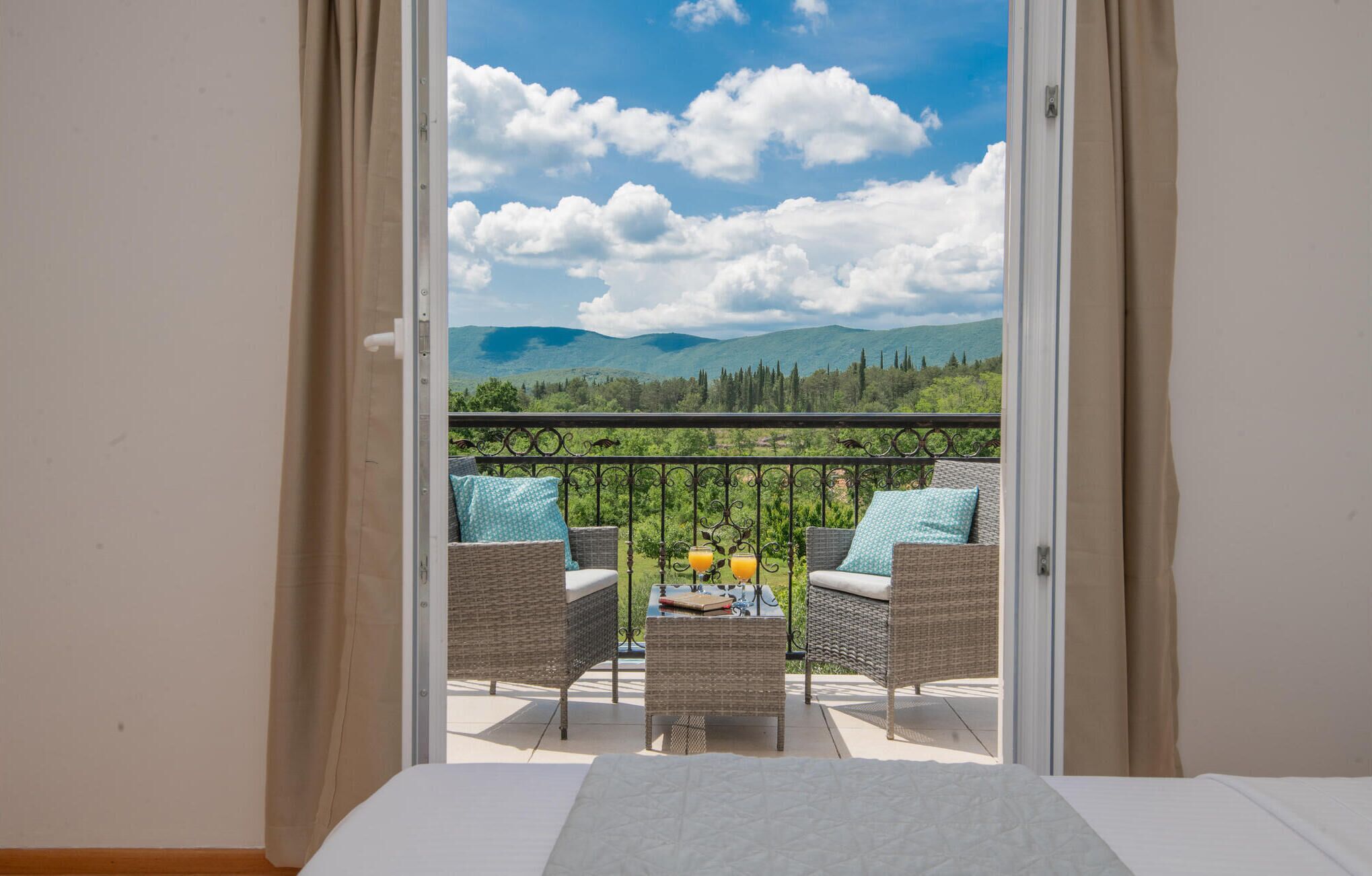 Ein Balkon mit Korbmöbeln und einem Tisch, der auf eine gebirgige Landschaft blickt.