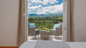 A balcony with wicker furniture and a table, overlooking a mountainous landscape.