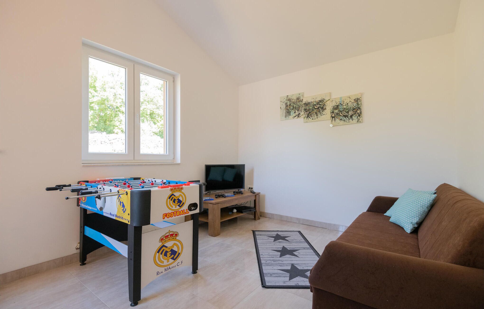 Ett vardagsrum med ett fotbollsspel, en tv, en soffa och konstverk på väggen.