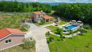 A two-story house with a swimming pool, stone pathway, and a view of the surrounding forest.