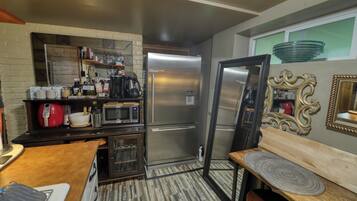 A compact kitchen with a refrigerator, microwave, and coffee maker. There is a wooden table with a bench and a decorative mirror on the wall.