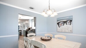 A dining area with a wooden table, white chairs, a chandelier, and a painting on the wall.