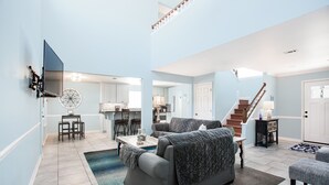 A spacious living room with a grey sofa, a coffee table, and a TV mounted on the wall.