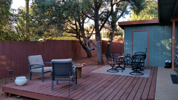 En udendørs terrasse med træterrasse, to stole, et bord og et lille skur.