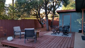 Une terrasse extérieure avec une plateforme en bois, deux chaises, une table et un petit abri de jardin.