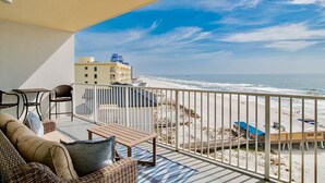 Ein Balkon mit Blick auf Strand und Meer, Korbmöbel und Geländer.