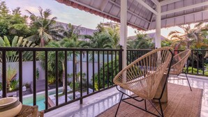 Un balcon agrémenté de fauteuils en osier, une piscine et une végétation tropicale luxuriante.