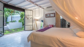 Un dormitorio con cama, mesita de noche, lámpara y vistas a un jardín.