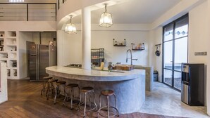 Une cuisine moderne dotée d’un îlot central, de tabourets de bar, d’appareils électroménagers en acier inoxydable et d’une grande fenêtre offrant une vue dégagée.