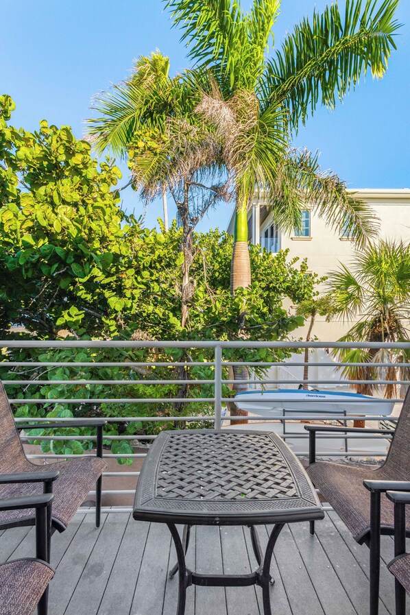 An outdoor seating area with a table and chairs, surrounded by lush greenery and a clear blue sky. - The Beach on Longboat Key #227 Resort by RVA (Longboat Key)