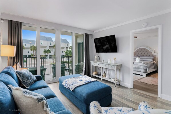 A modern hotel room with a balcony, a TV mounted on the wall, a bed with a headboard, and a white console table with decorative items.