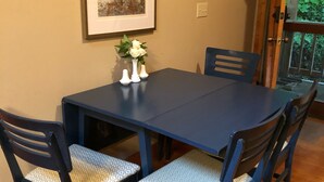 Una mesa de comedor con cuatro sillas, una obra de arte enmarcada en la pared y un florero con flores sobre la mesa.