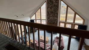 Una habitación con techo inclinado, chimenea de piedra y ventanas amplias que ofrecen vistas al exterior.