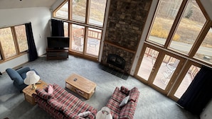 Un salón amplio con chimenea de piedra, ventanas grandes y un rincón de descanso acogedor.