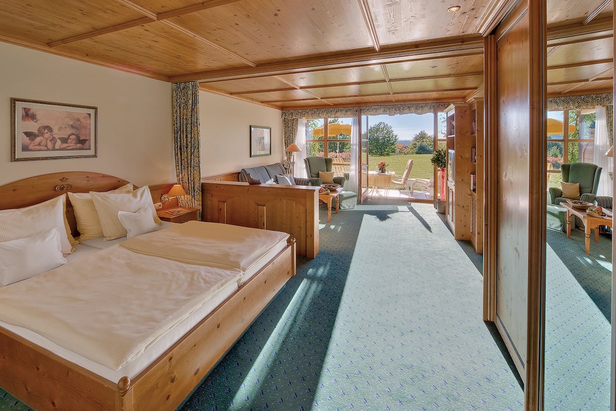 A wooden bedroom with a large bed, a nightstand, a chair, and a view of the outdoors.