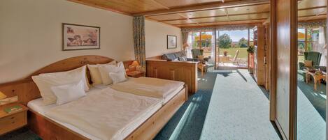 A wooden bedroom with a large bed, a nightstand, a chair, and a view of the outdoors.