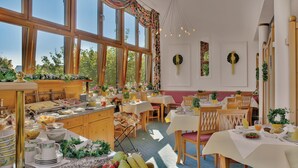 A bright dining area with large windows, a buffet setup, and a variety of table settings. - Aparthotel am Sonnenhuegel (Bad Birnbach)