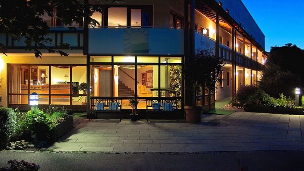 A two-story building with large windows, a bench outside, and a staircase leading to the upper floor. - Aparthotel am Sonnenhuegel (Bad Birnbach)