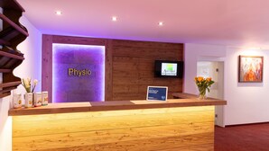 A reception desk with a wooden finish, a sign reading "Physio," and a television screen. - Aparthotel am Sonnenhuegel (Bad Birnbach)