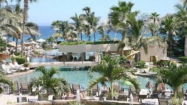 A resort pool area with multiple pools, palm trees, and lounge chairs.