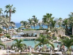 Área de piscina do resort com várias piscinas, palmeiras e espreguiçadeiras.