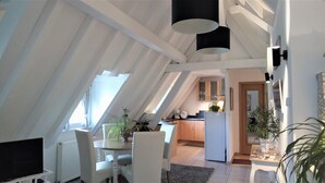 En modern lägenhet i loftstil med ett sluttande tak, en matplats med vita möbler och ett kök med träskåp.