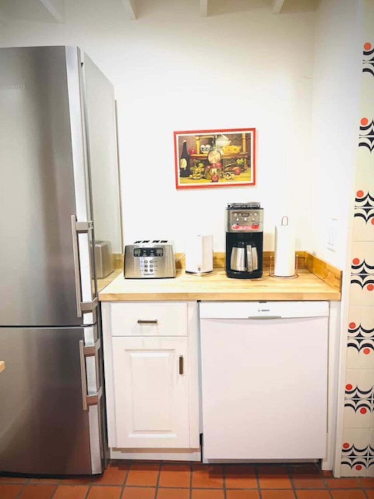 A compact kitchen with a stainless steel refrigerator, a coffee maker, a toaster, and a dishwasher.