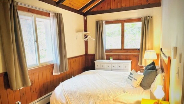 Une chambre avec un grand lit, des murs en bois, une commode et une fenêtre avec des rideaux.