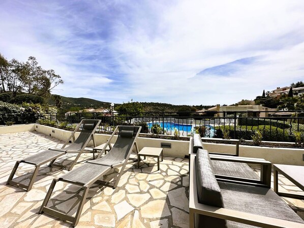 A rooftop pool area with lounge chairs and a view of a swimming pool.