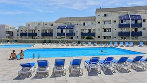 A swimming pool area with lounge chairs and a building with solar panels.
