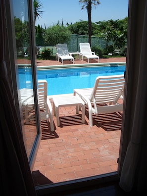 A pool area with white lounge chairs and a table, surrounded by a brick patio. - La Tipasa (Tateyama)