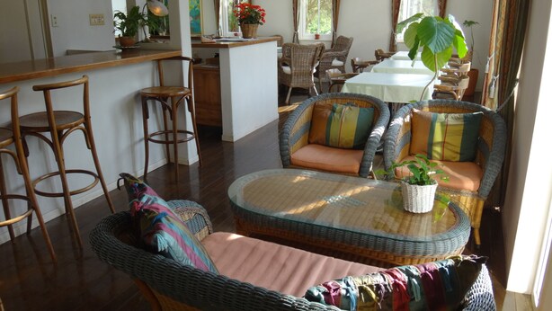 A spacious living area with a central seating area featuring a wicker sofa and a round coffee table. There are multiple chairs and a dining table in the background. - La Tipasa (Tateyama)