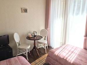 A hotel room with two single beds, a small table with a coffee maker and a basket, two wicker chairs, a television on a stand, and a window with curtains. - La Tipasa (Tateyama)