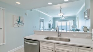 A modern kitchen with a large island, stainless steel appliances, and a view to the living area. - Seawind 1007 | Updated condo with perfect beach view and walk to dine, shop, more! (Gulf Shores)