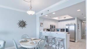 A modern kitchen with white cabinets, stainless steel appliances, and a central island with bar stools. - Seawind 1007 | Updated condo with perfect beach view and walk to dine, shop, more! (Gulf Shores)