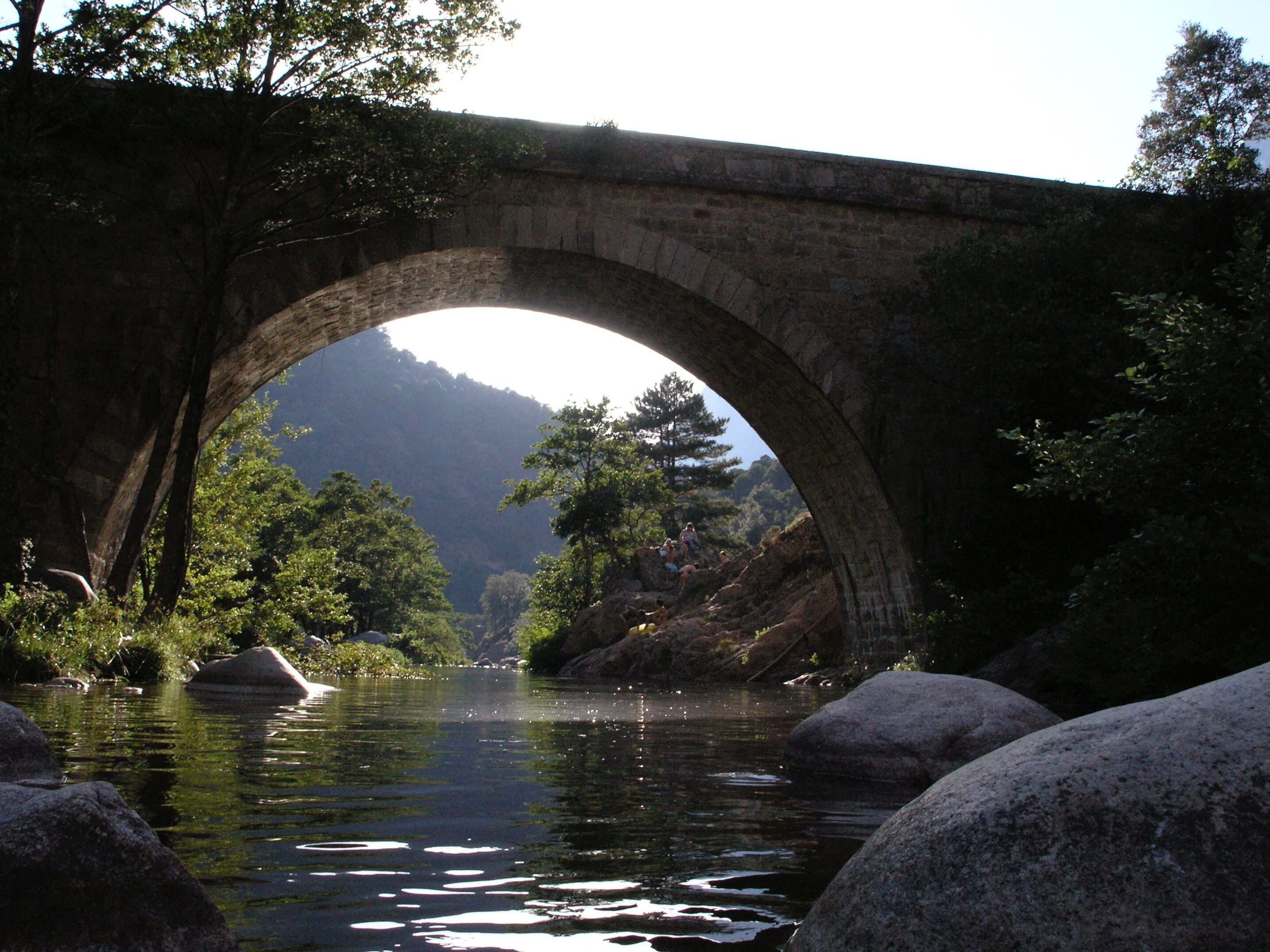 A stone bridge over a river with trees and hills in the background.