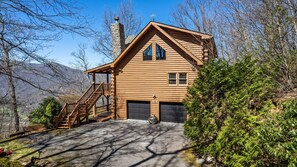 Cozy cabin with a prominent chimney and steeply pitched roof, featuring a front porch and wooden staircase.