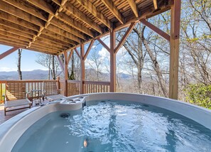 Relax on the deck with a soothing hot tub overlooking the surrounding mountains and lush trees.