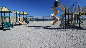 Une aire de jeux avec plusieurs toboggans et des structures d’escalade, le tout situé sur une plage de sable.