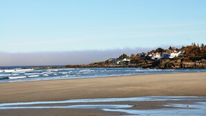 Une plage avec un rivage rocheux, des vagues et des maisons situées sur une colline.
